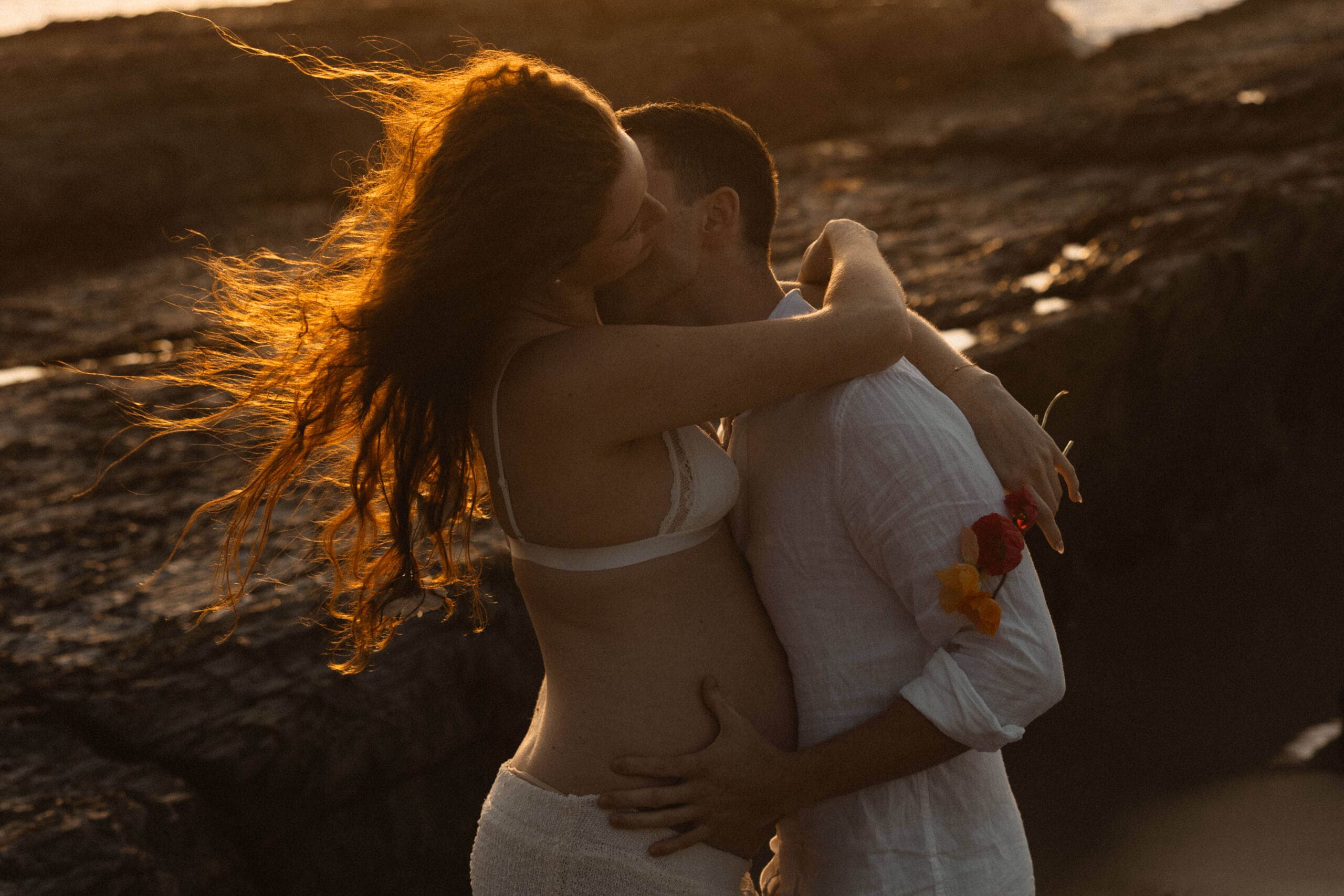 pregnant couple embracing by the ocean as the sun sets