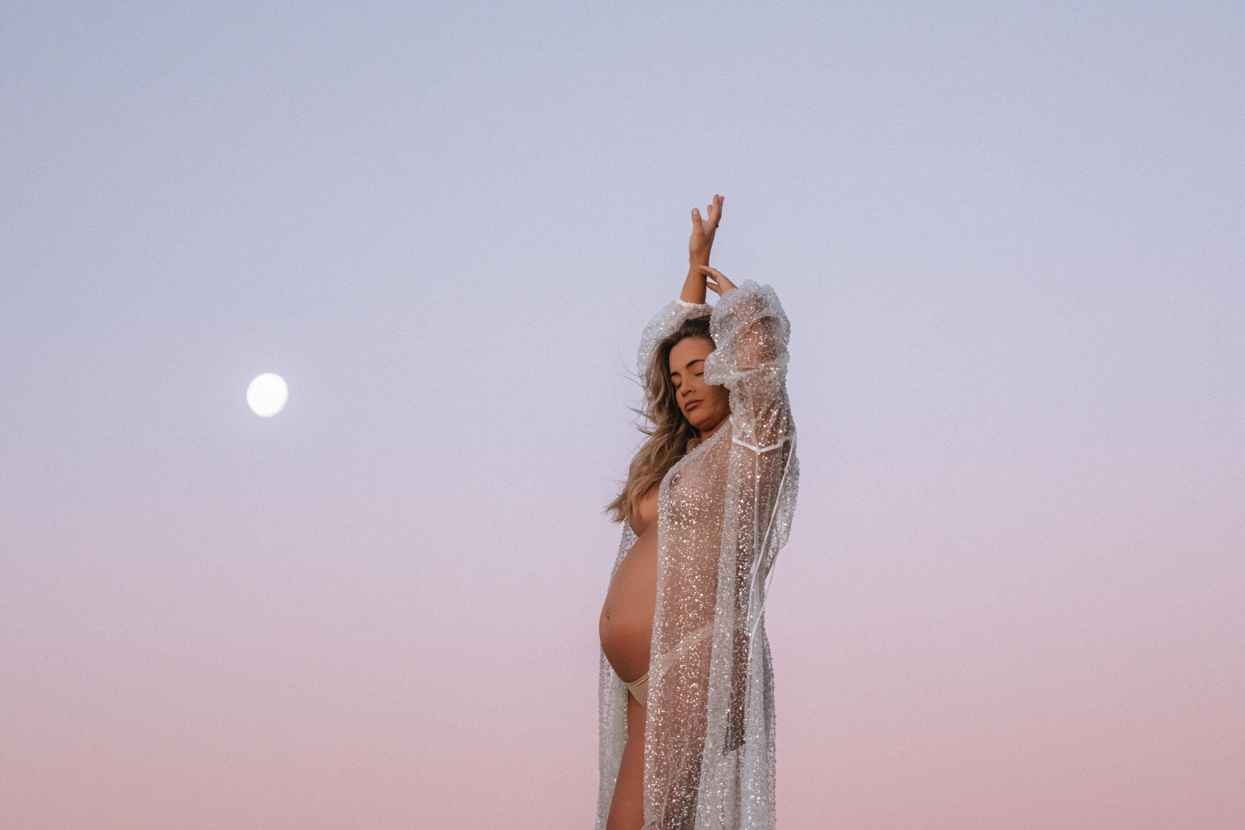 Mother to be arms reaching up to the full moon at blue hour